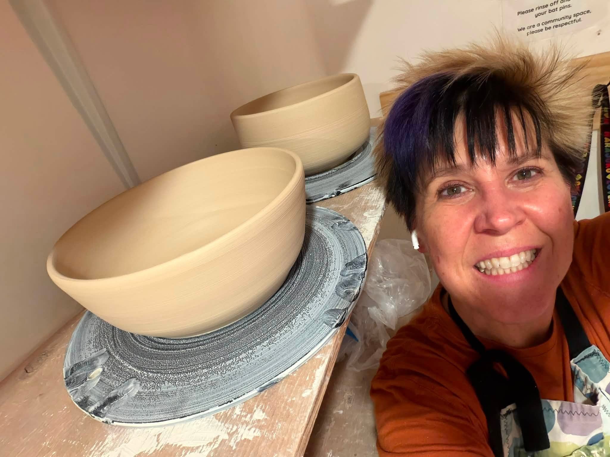Kellie in the pottery studio, smiling beside two freshly thrown bowls on the workbench.